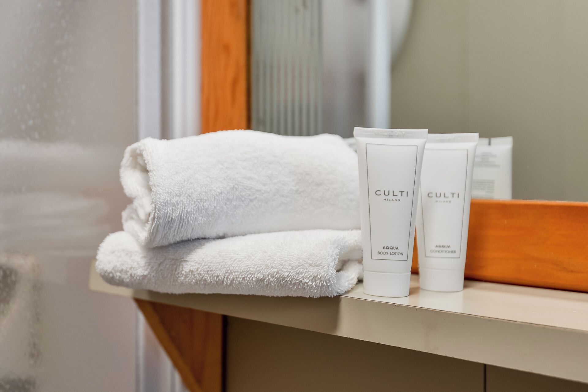Een badkamer met een witte handdoek, twee flesjes bodylotion en een spiegel.