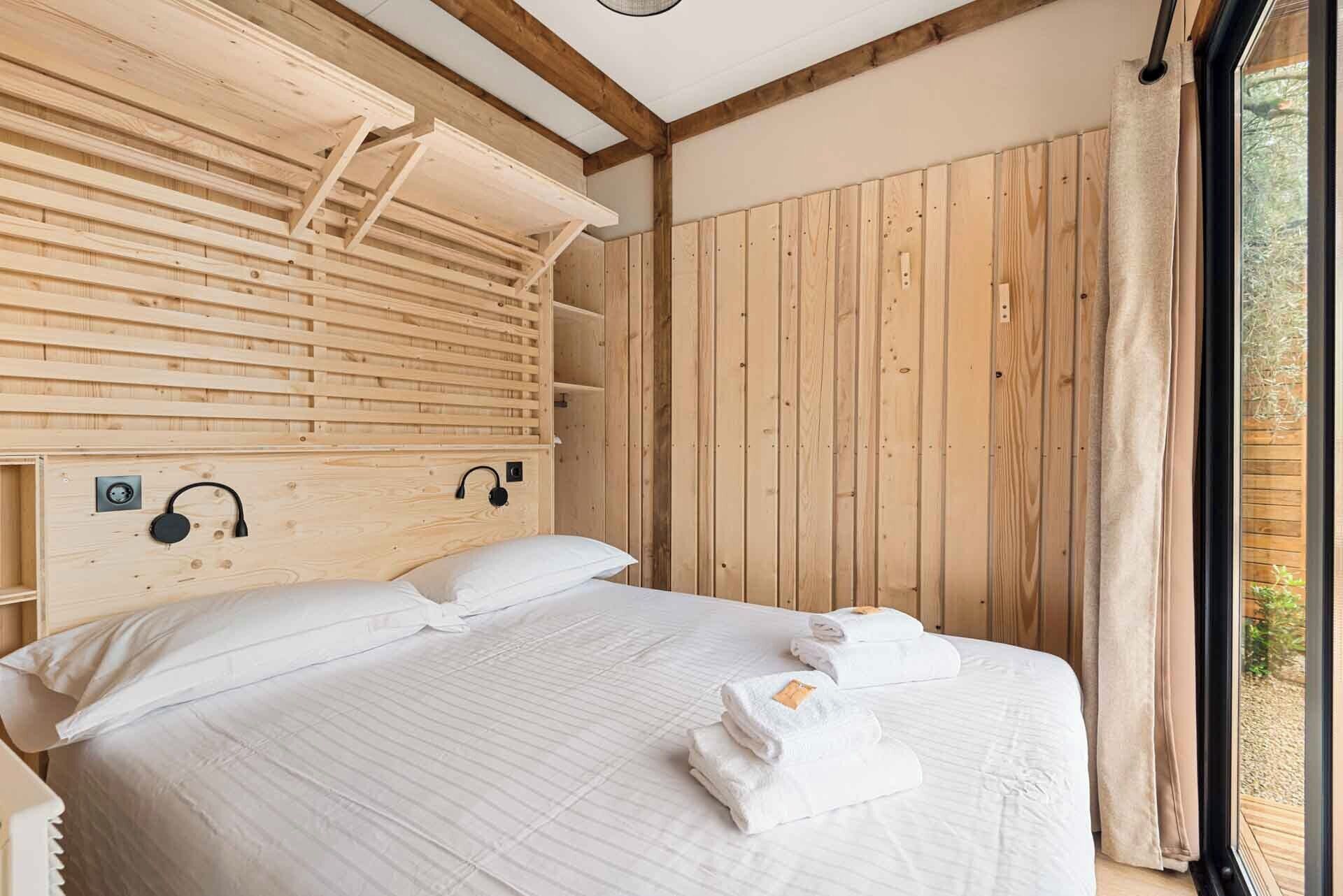 A wooden cabin-style bedroom with a bed, pillows, and towels.