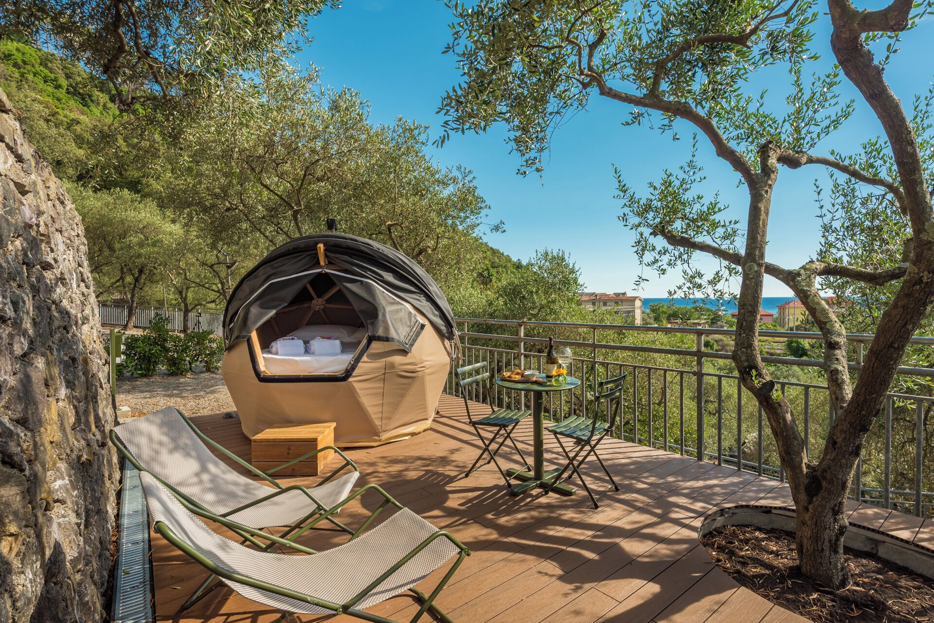 A cozy outdoor sleeping pod with a table and chairs, surrounded by trees and a wooden deck.