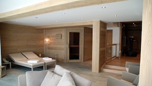 Une salle de spa moderne avec des murs en bois, une table de massage, un canapé et une porte en verre donnant sur un espace douche.