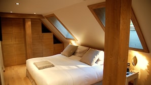 Une chambre à coucher avec un grand lit, une armoire en bois et des fenêtres intégrées dans un plafond en pente.