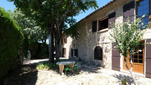 Un edificio de piedra con un patio, un banco y un árbol.