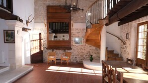 Un interior rústico con pared de piedra, escalera de madera y comedor con una mesa grande y sillas.