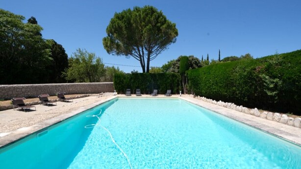 Una piscina rectangular con agua azul cristalina, rodeada por un muro de piedra y un seto.