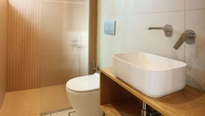 Et moderne badeværelse med et hvidt toilet, en trækommode og en stor, hvid vask.
