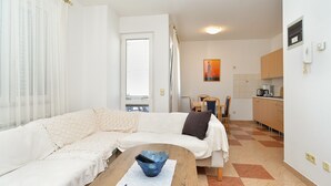 Ein kompakter Wohnbereich mit einer Couch, einem kleinen Esstisch, einer Küchenzeile und einem Fenster mit Jalousien.
