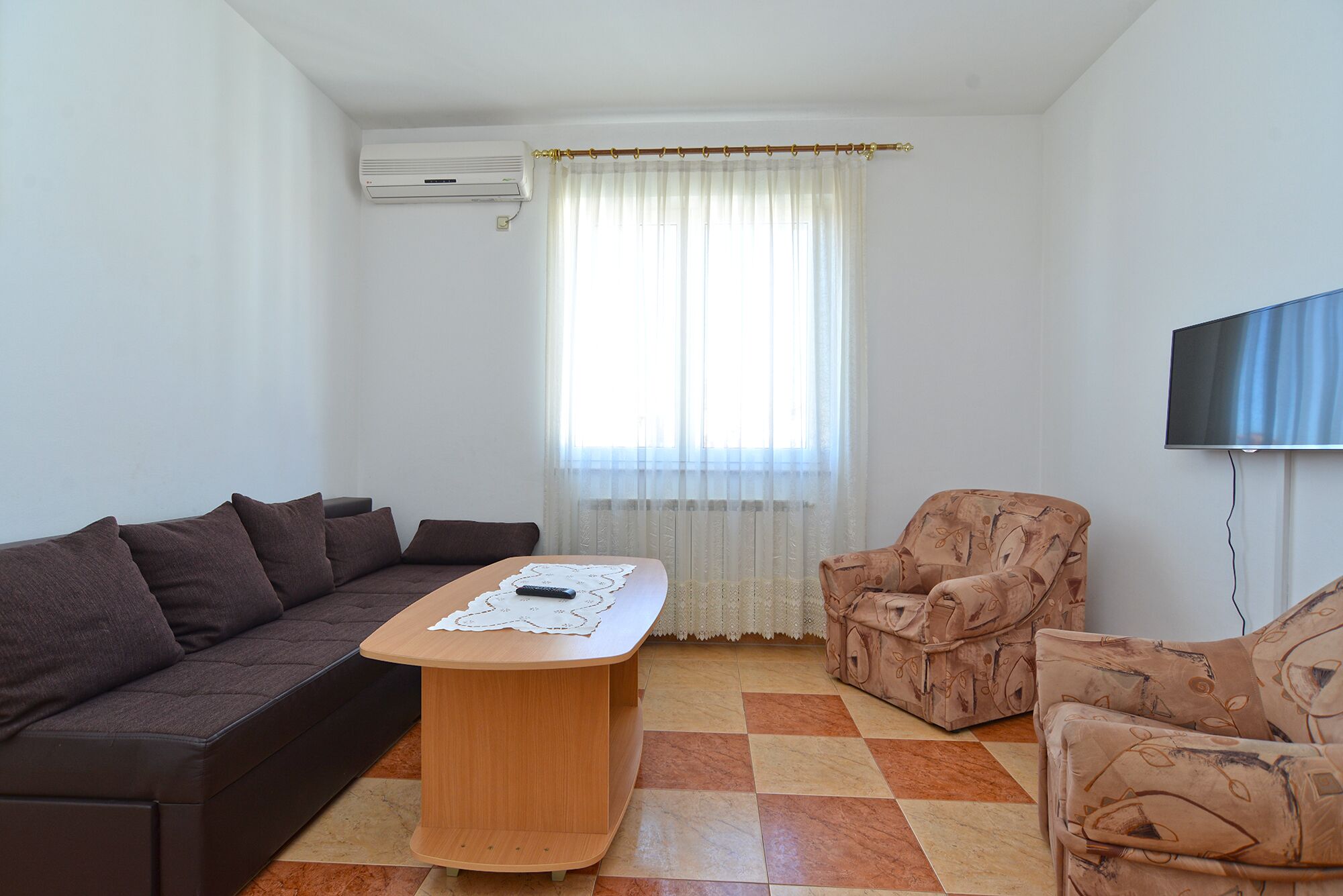 A living room with a sofa, a coffee table, a patterned armchair, and a television.