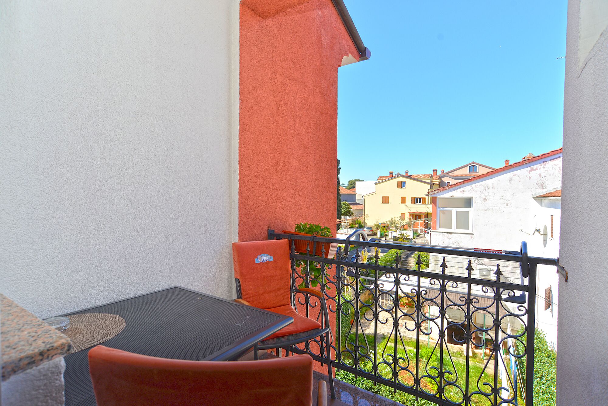 Un balcone con tavolo e sedie, un piccolo giardino e vista sugli edifici circostanti.