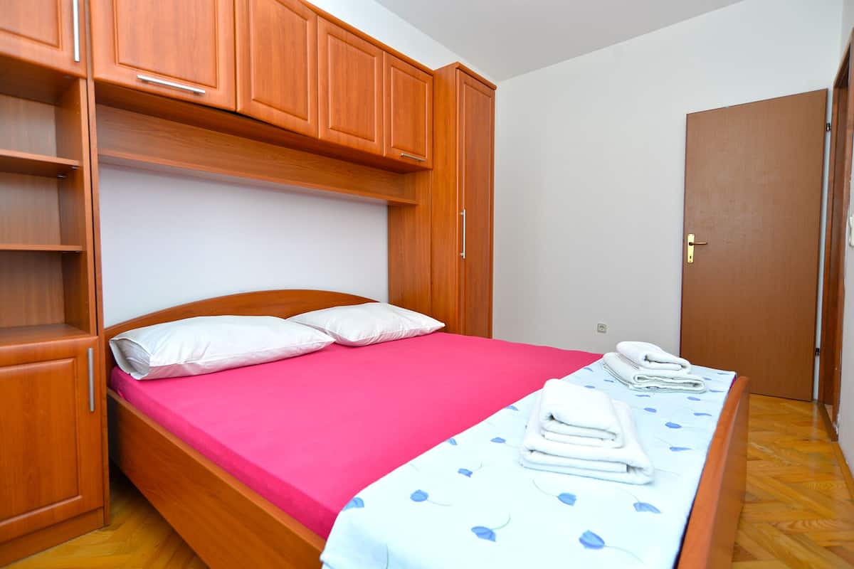 A compact bedroom with a single bed, wooden wardrobe, and a door.