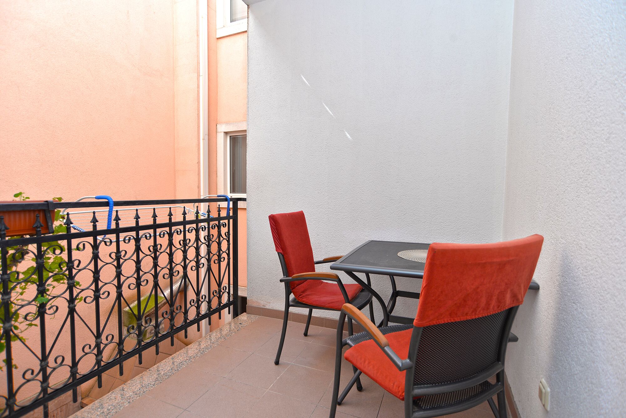 A small outdoor seating area with two chairs and a table, a black wrought iron fence, and a white wall.