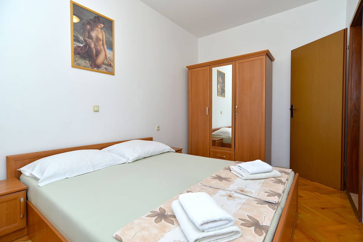 A bedroom with a bed, a wooden wardrobe, a mirror, and a painting on the wall.