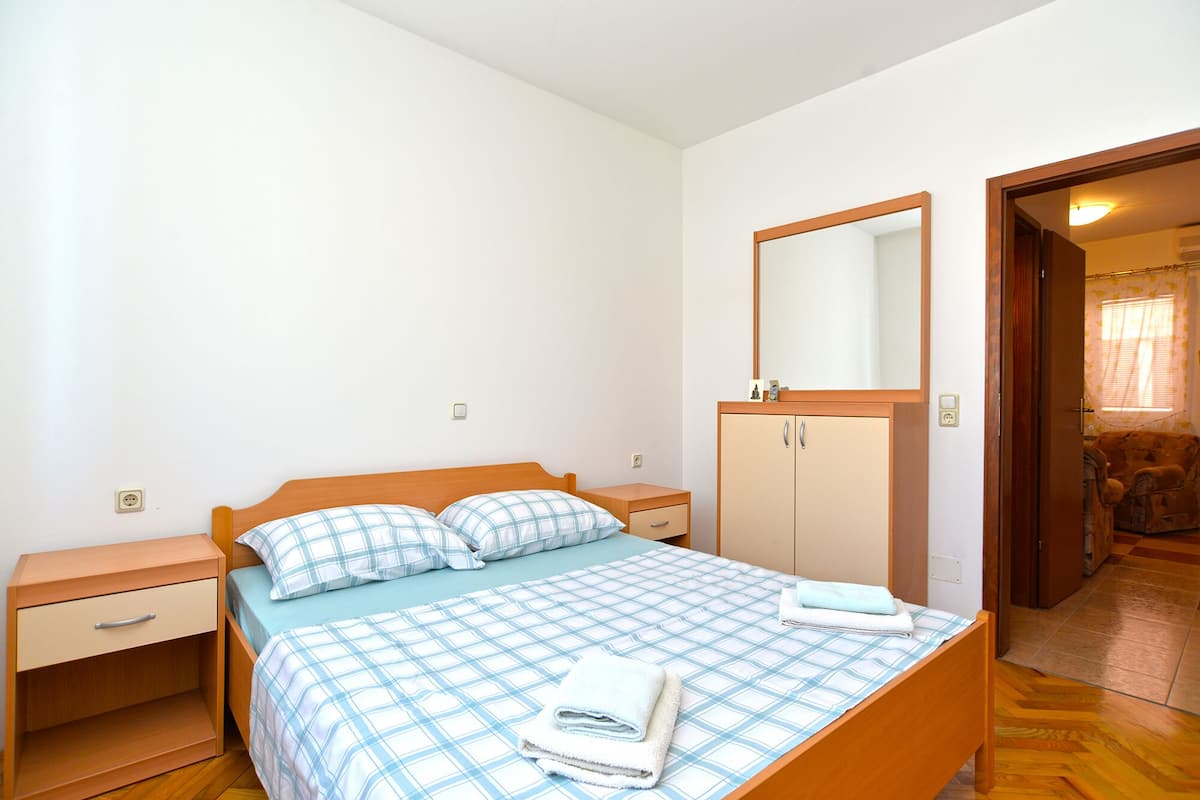 A bedroom with a bed, a nightstand, a wardrobe, and a door leading to another room.