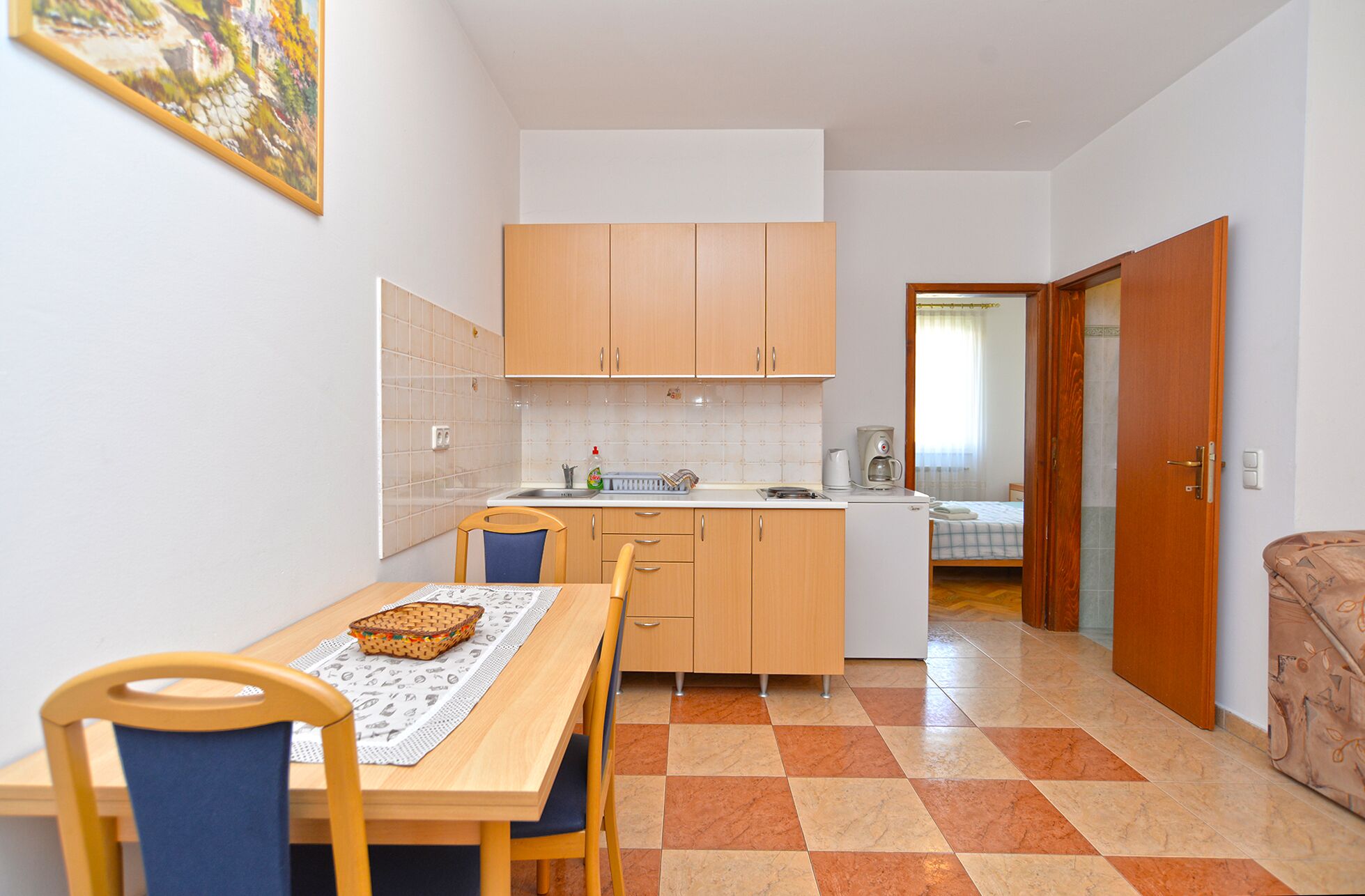 A compact kitchen with wooden cabinets, a dining table with chairs, and a checkered floor.
