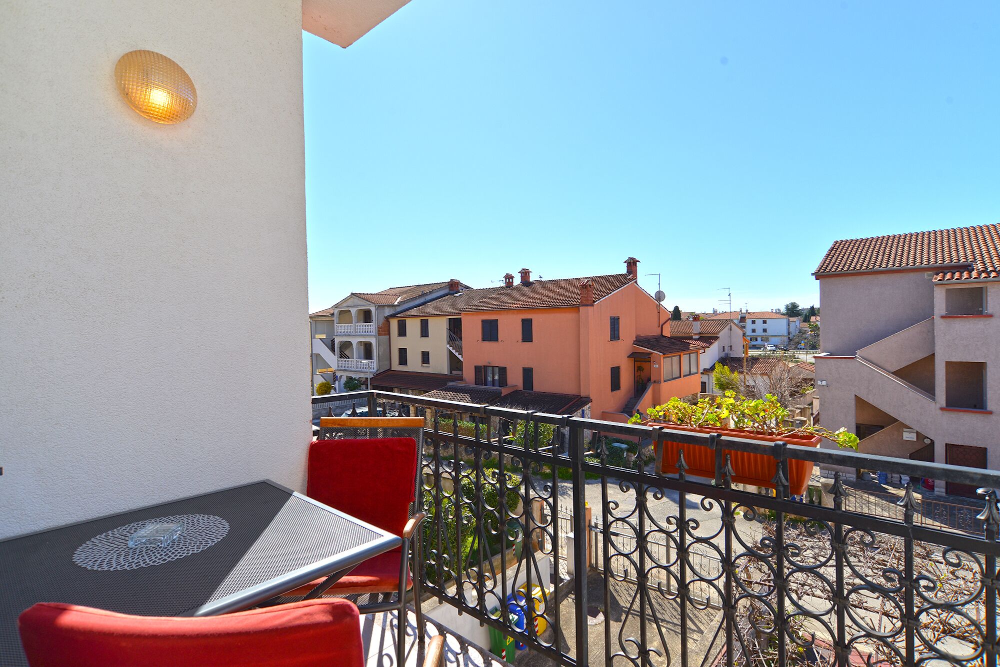 Ein Balkon mit Tisch und Stühlen, einer Brüstung und Blick auf Gebäude im Hintergrund.