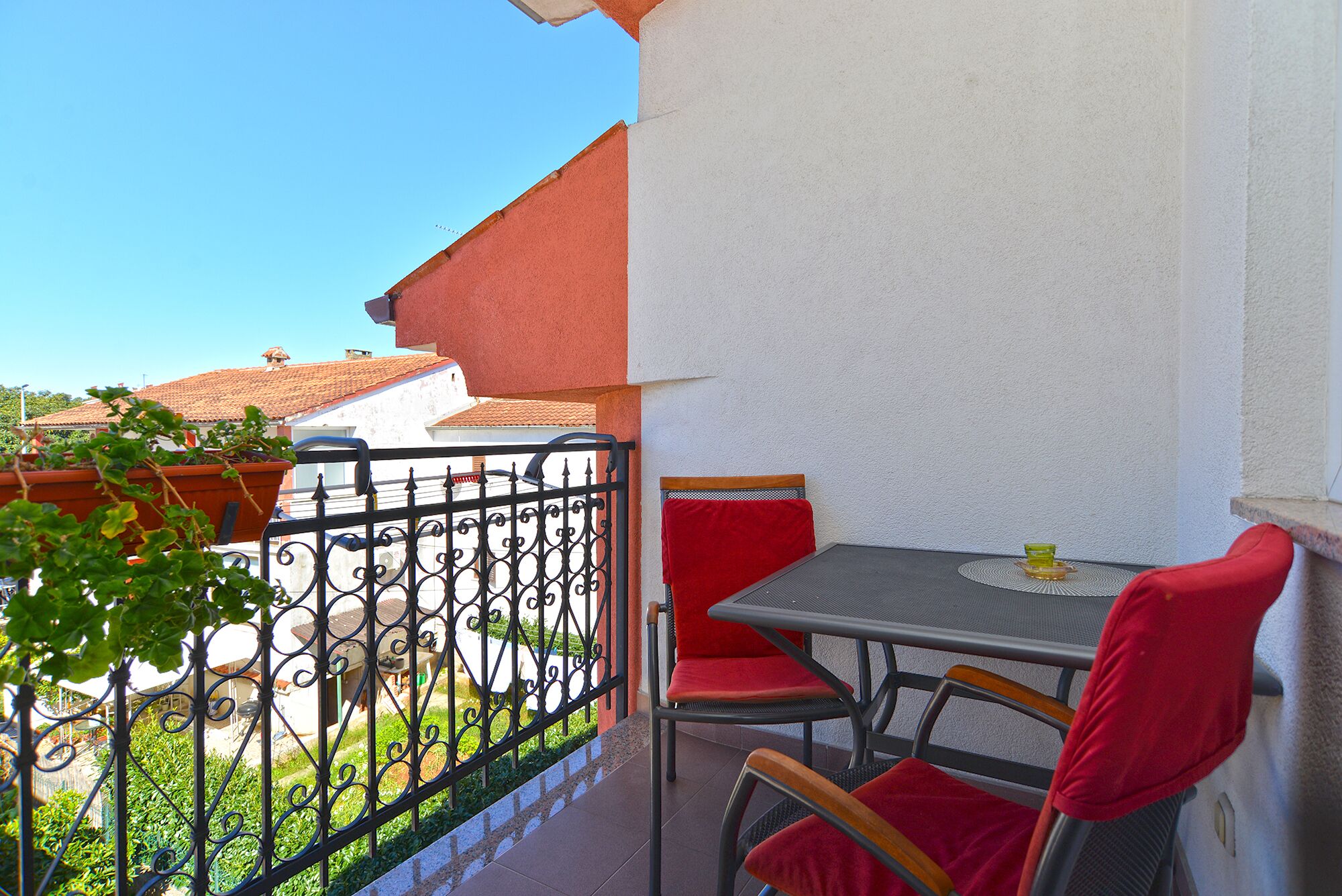 A balcony with a table and chairs, a railing, and a view of buildings and greenery.
