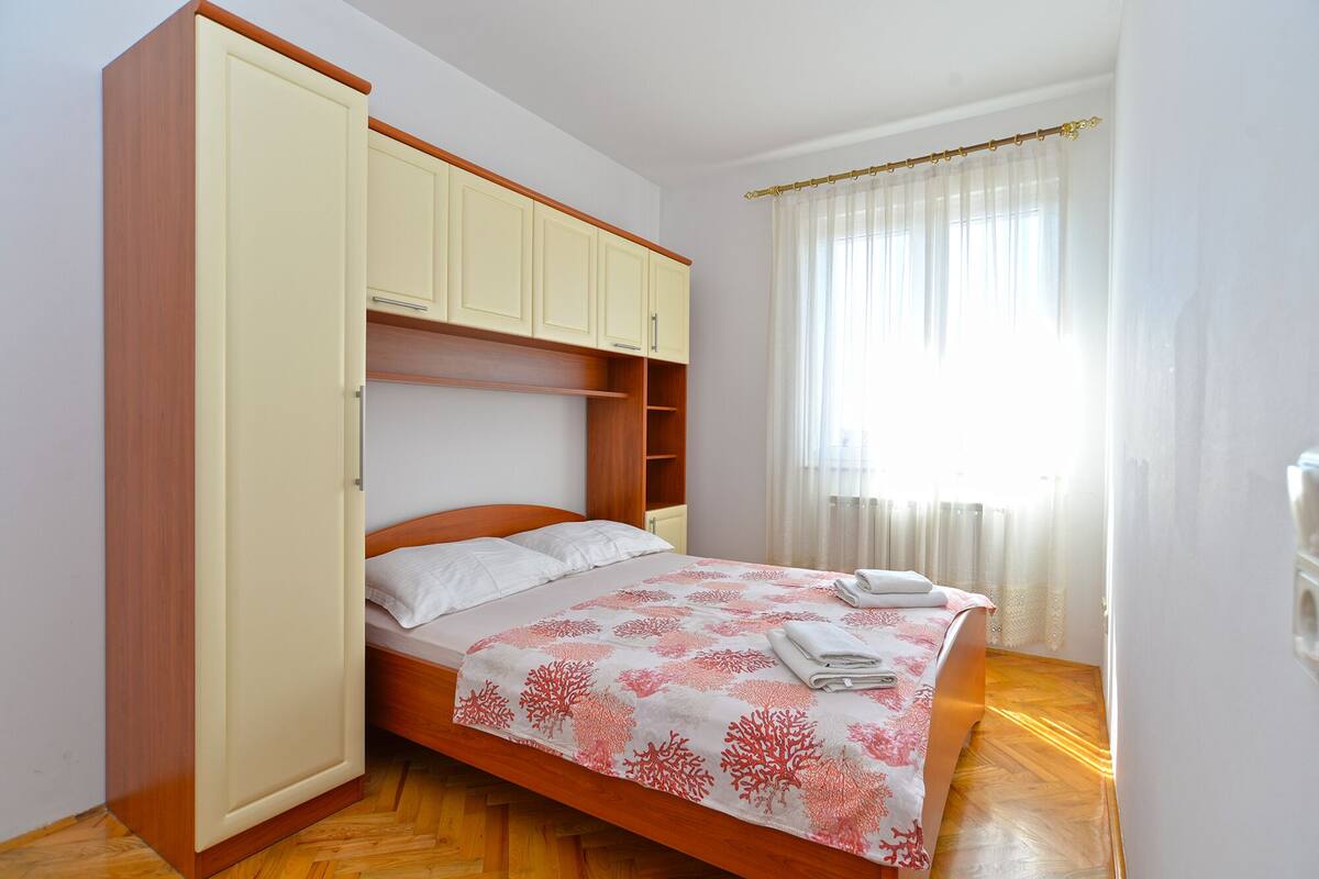 A bedroom with a bed, wooden wardrobe, and a window with curtains.