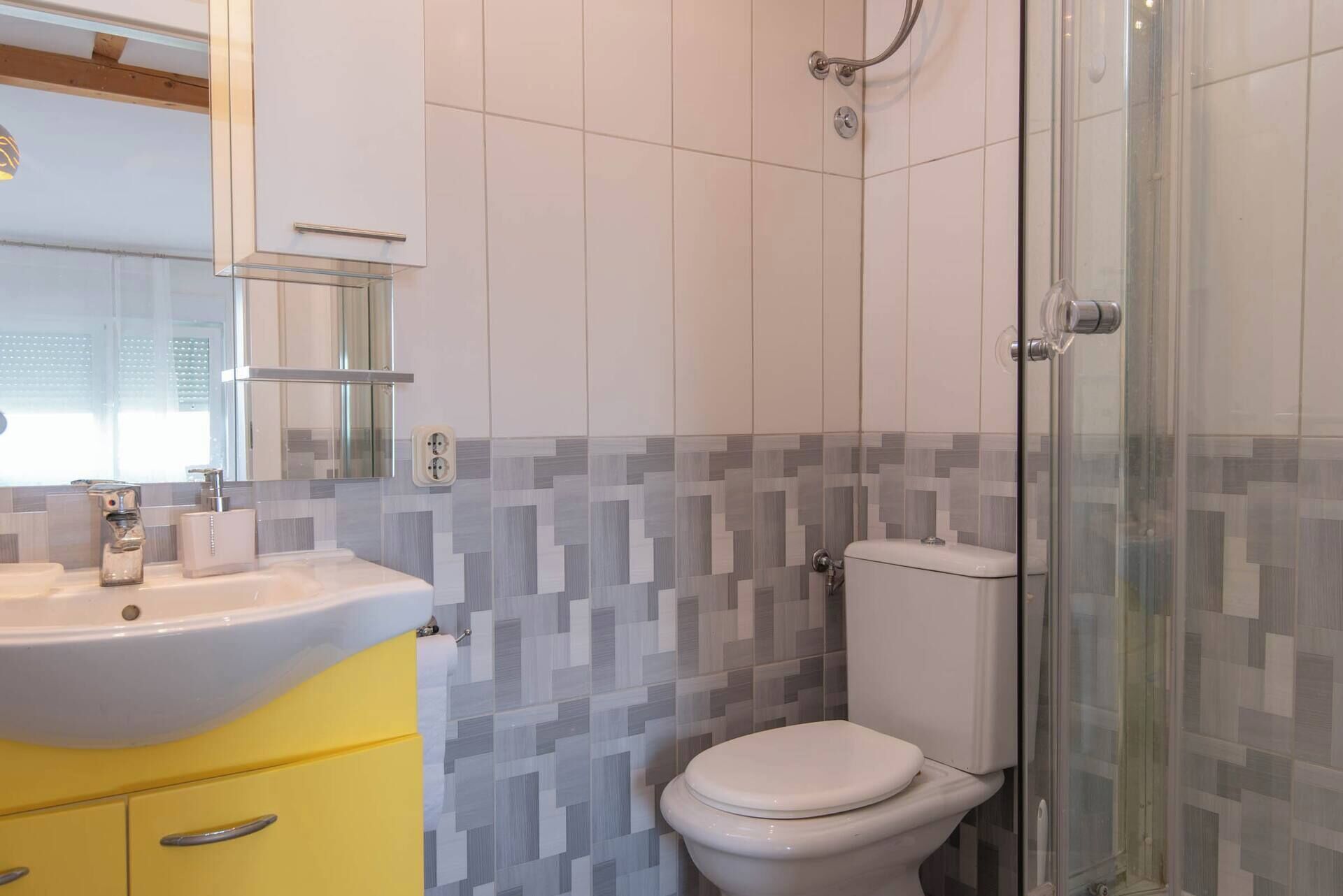 Ein Badezimmer mit einem gelben Waschtisch, einem weißen Waschbecken, einer Toilette und einer Duschkabine.