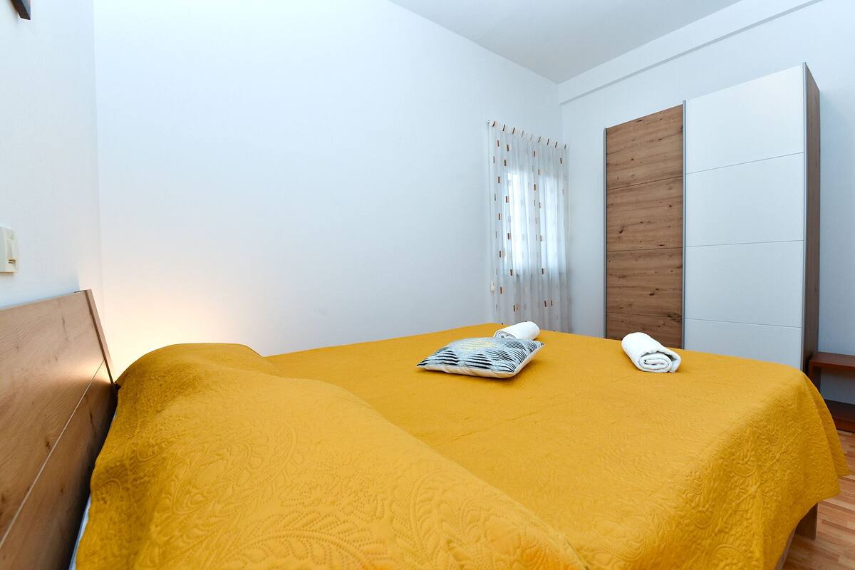 A room with a bed covered in yellow bedding, a pillow, and a rolled towel.