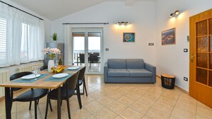 Un comedor con una mesa dispuesta para dos personas, un sofá y vistas al balcón exterior a través de un ventanal.