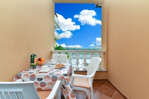 A balcony with a table set for two, featuring a tablecloth with a polka dot pattern, white chairs, and a view of a building and sky through a window. - Apartments 2310 (Vodnjan)