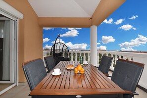 Un balcone con un tavolo di legno, due sedie, una sedia a dondolo e vista sul cielo e sugli edifici in lontananza.