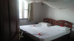 A neatly made bed with white linens and decorative floral arrangements, a wooden headboard, and a window with curtains. - JOHARI VILLA (Malindi)