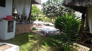 A courtyard with thatched-roof huts, a small palm tree, and outdoor furniture. - JOHARI VILLA (Malindi)