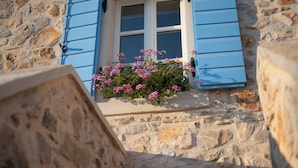 A stone building with a window featuring blue shutters and pink flowers in the window sill. - Heritage Vila malena (Vir)
