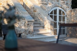 Una escalera de piedra que lleva a una puerta blanca con ventana, rodeada de muros de piedra.
