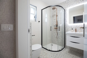 Un baño moderno con ducha de vidrio, inodoro blanco y tocador con espejo.
