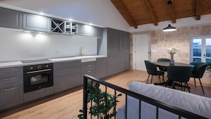 A modern kitchen with grey cabinets, a built-in oven, and a dining area with a table and chairs. - Heritage Vila malena (Vir)