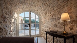 A stone-walled room with a large arched window, a table with a lamp, and a bench. - Heritage Vila malena (Vir)