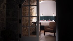 A room with a stone wall, a bed with floral bedding, a chair, and a table with a lamp. - Heritage Vila malena (Vir)