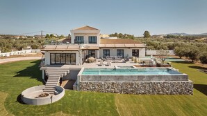Ein modernes, zweistöckiges Haus mit Swimmingpool, Sitzgelegenheiten im Freien und einer Steinmauer.