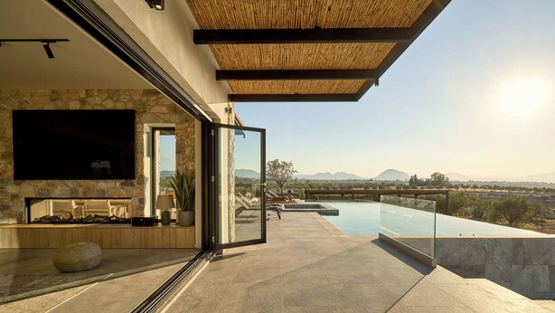 Ein moderner Außenbereich mit Steinmauer, Flachbildfernseher und Pool mit Blick auf eine reizvolle Landschaft.