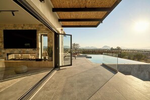 Un espace de vie extérieur moderne, doté d’un mur en pierre, d’un téléviseur à écran plat et d’une piscine offrant une vue panoramique sur un paysage magnifique.