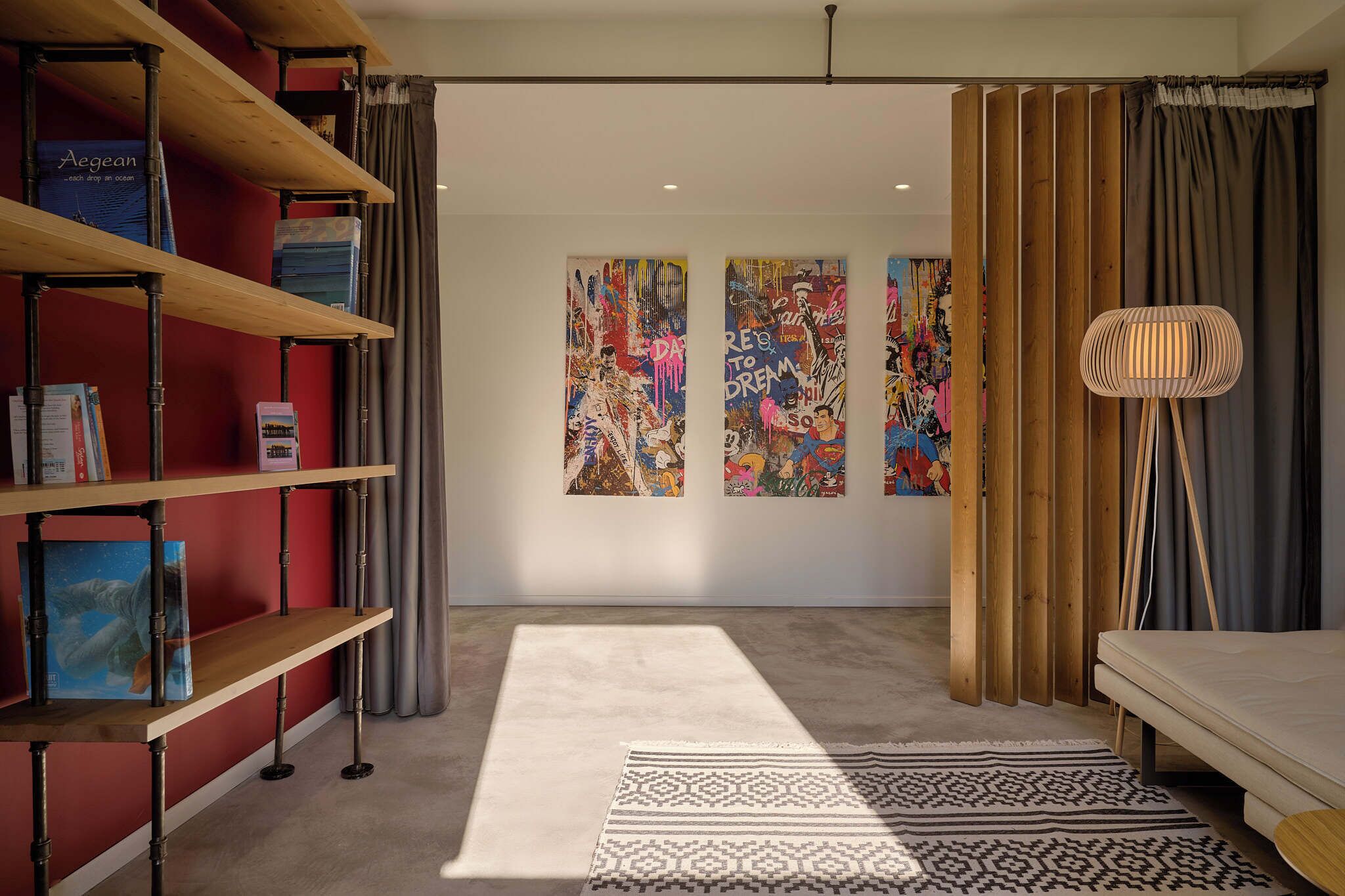 A modern room with a red wall, a wooden bookshelf, a patterned rug, and abstract art on the wall.