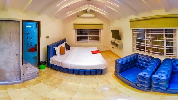 A spacious room with a large bed, a blue sofa, and a shower area. - Tectona Treetop Mansion (Hyderabad)