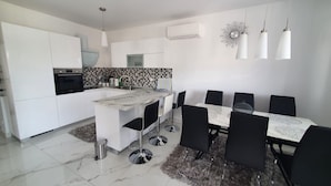Uma cozinha moderna com armários brancos, uma ilha central e uma área de jantar com mesa e cadeiras.