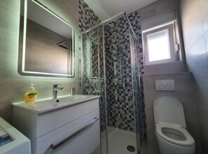 Un baño con ducha de mampara de vidrio, un lavamanos blanco con espejo y un inodoro.