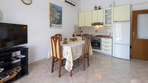 A compact kitchen with a dining area, a TV, and a clock on the wall. - Bright and Spacious Apartment With Terrace in Kastel Stafilic (Kastela)