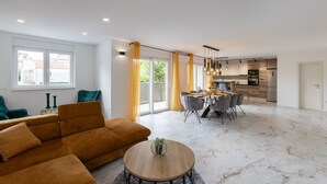 Ein modernes Wohnzimmer mit einer Couch, einem Esstisch und einer Küche im Hintergrund.
