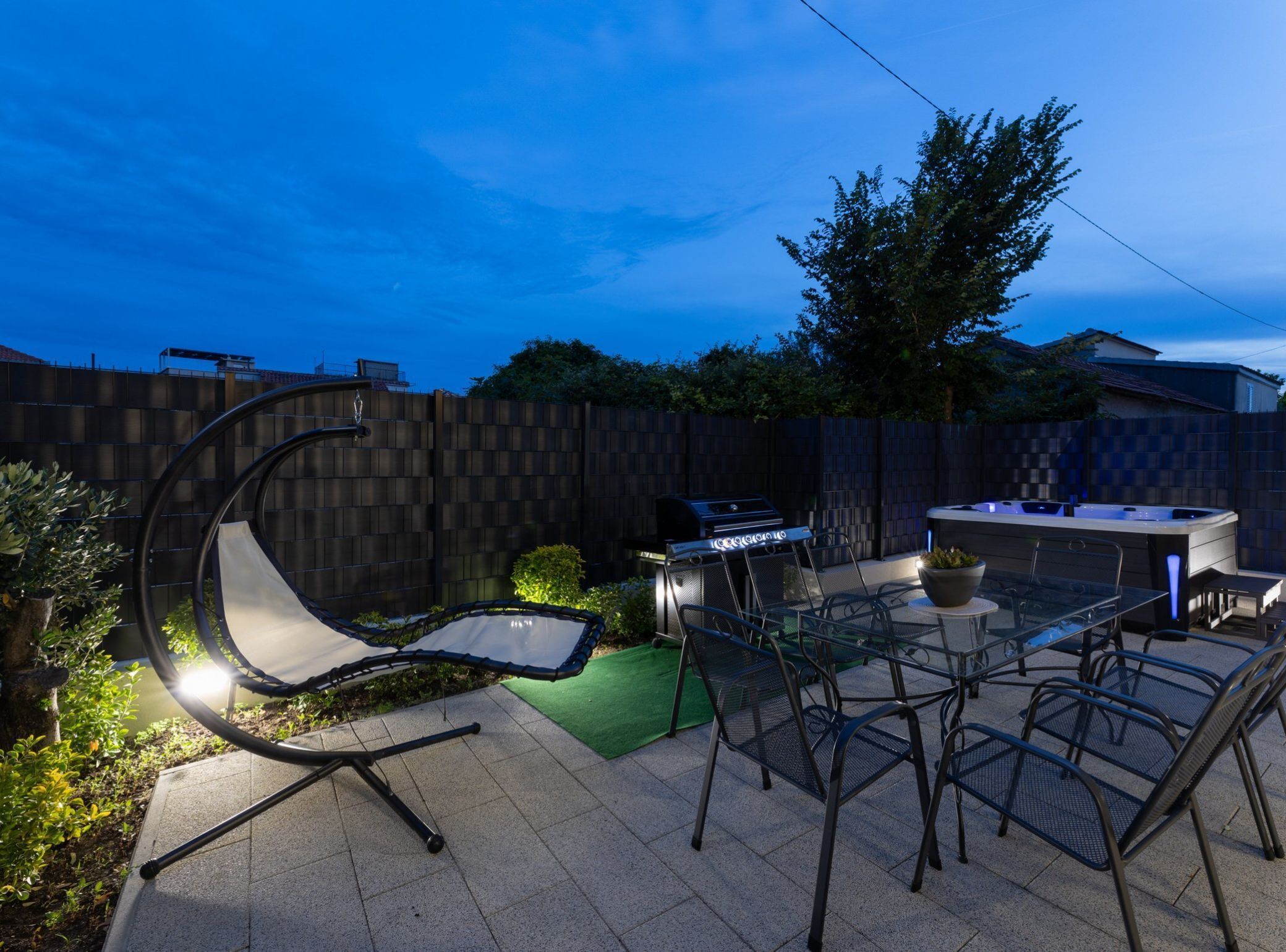 En utomhusplats med en terrass, en bubbelpool, en grill och moderna stolar i metall.