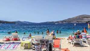 A beach with clear blue water, people swimming, and sun loungers on the sand. - Holiday Home by the Sea With Terrace & Ocean Views on Čiovo (Okrug)