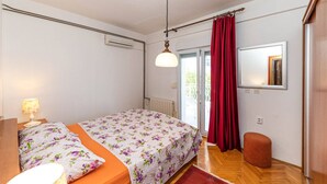 A bedroom with a bed, a nightstand, a lamp, a red curtain, a wooden floor, and a window with a view. - Holiday Home by the Sea With Terrace & Ocean Views on Čiovo (Okrug)