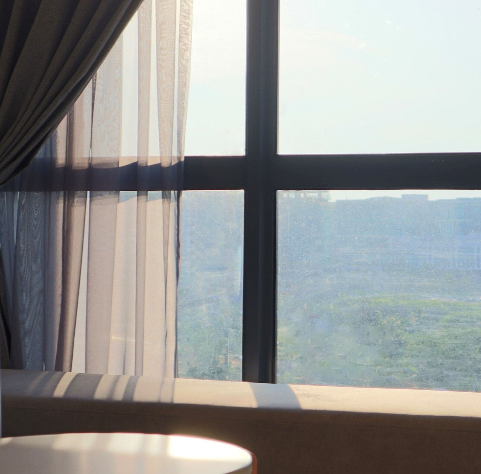 A room with a large window, sheer curtains, and a view of a cityscape.