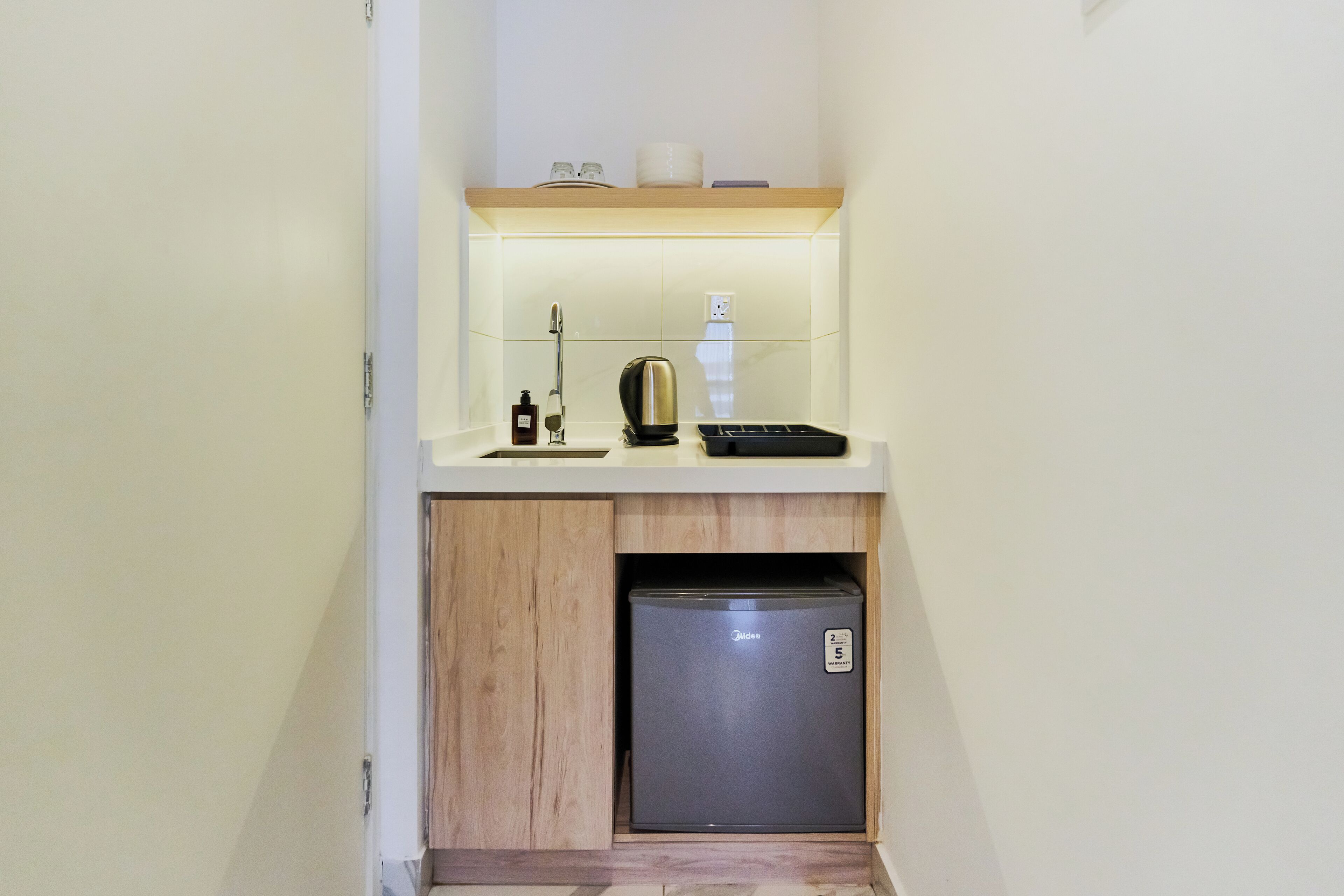 A compact kitchenette with a built-in refrigerator, a coffee maker, and a small shelf above the counter.
