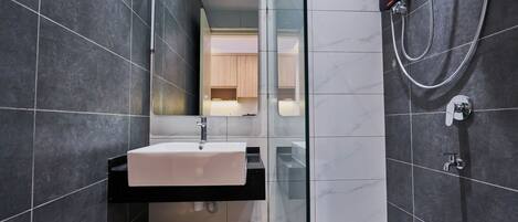 A modern bathroom with dark tiles, a white sink, a glass shower enclosure, and a visible mirror.