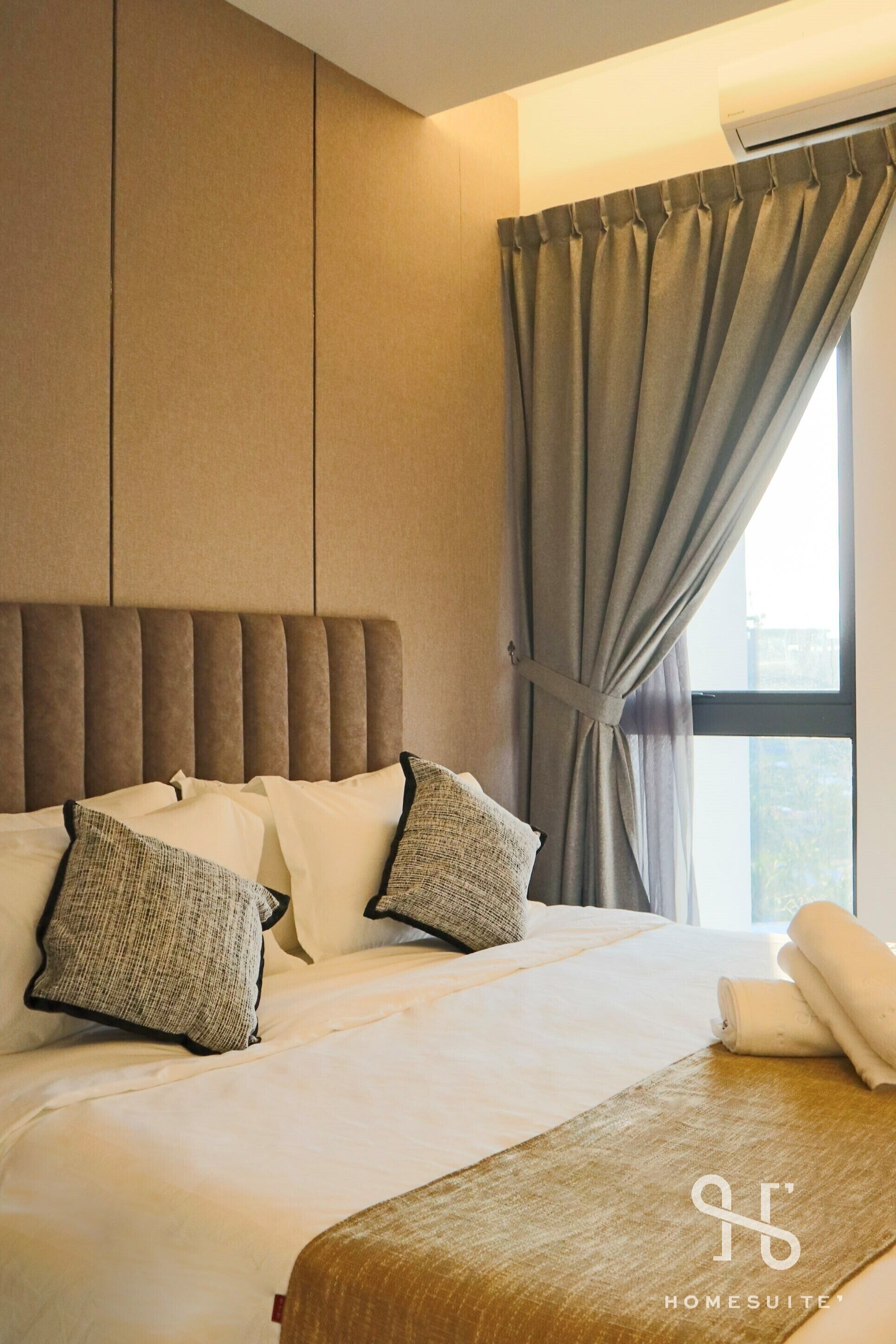 A neatly made bed with a headboard, pillows, and a rolled towel.