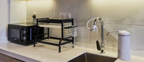 A kitchen with a built-in microwave, a black wire rack, a white coffee maker, and a stainless steel sink.